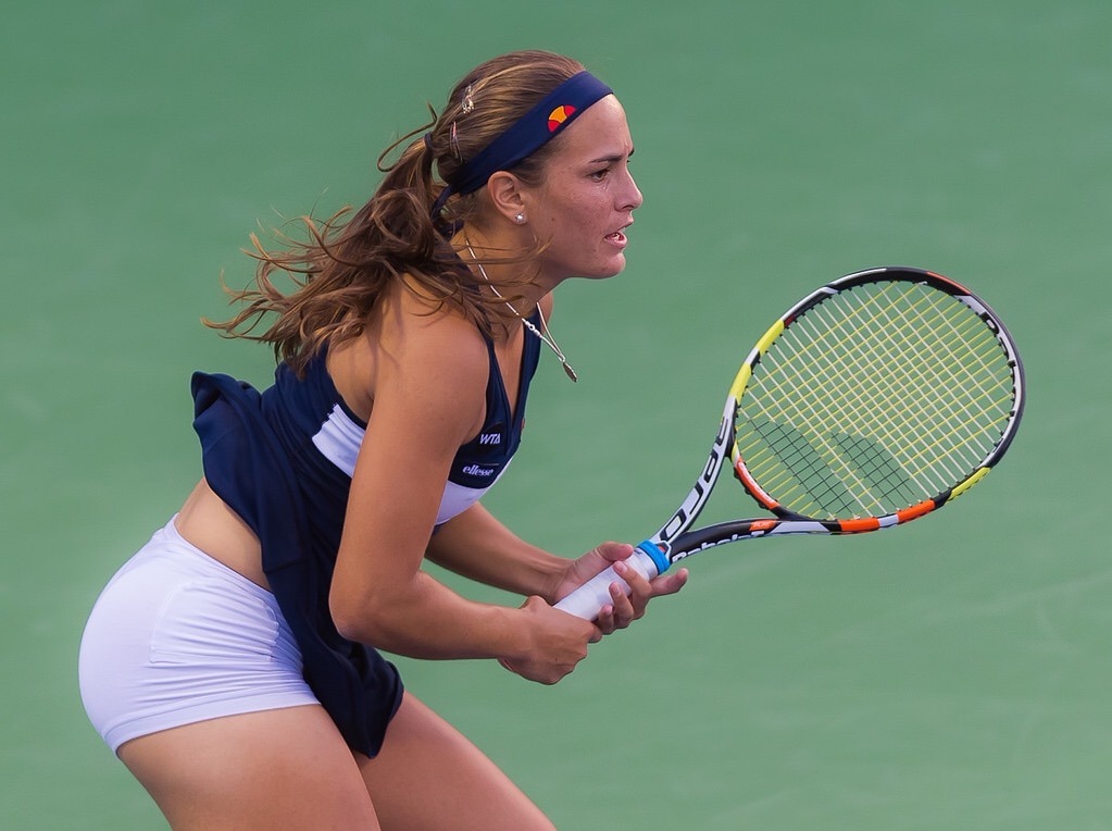 Een tennisspeelster in sportkleding maakt zich klaar om een slag terug te slaan op een hardcourt, terwijl ze haar racket met beide handen vasthoudt.