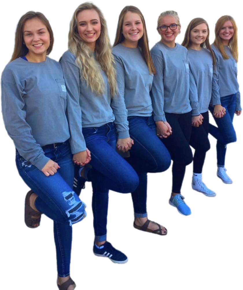 Zes jonge vrouwen staan op een rij, elk met hun rechterbeen omhoog en houden elkaars hand vast. Ze dragen allemaal een blauwe spijkerbroek en bijpassende grijze shirts met lange mouwen.