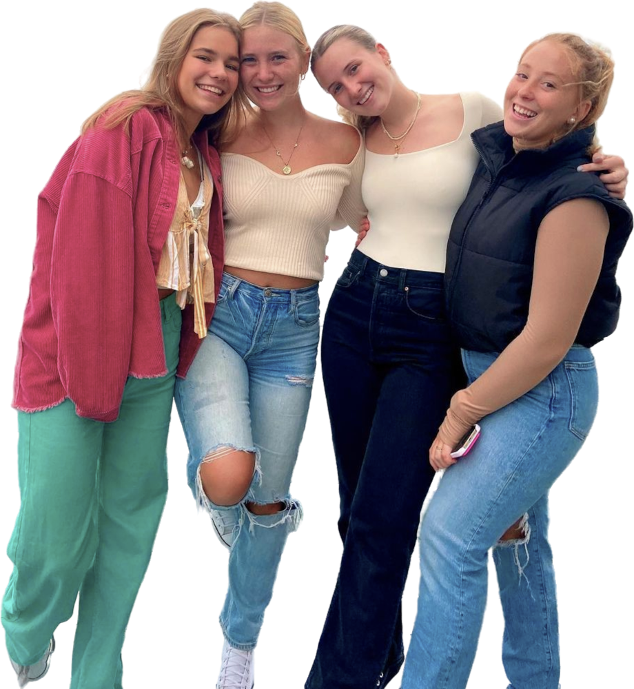 Vier vriendinnen bij elkaar. Ze hebben de armen over elkaars schouder en kijken de camera in. Een meisje heeft een smartphone in haar hand.